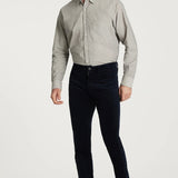 Man wearing a light gray button-up shirt, dark blue jeans, and brown shoes on a white background