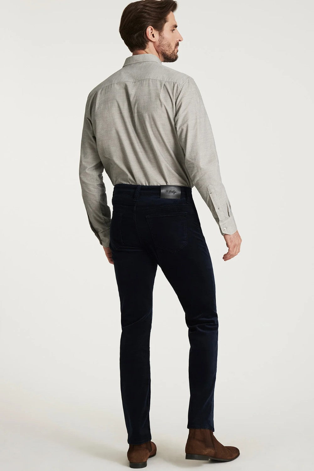 Man wearing a light gray shirt and dark jeans on a white background
