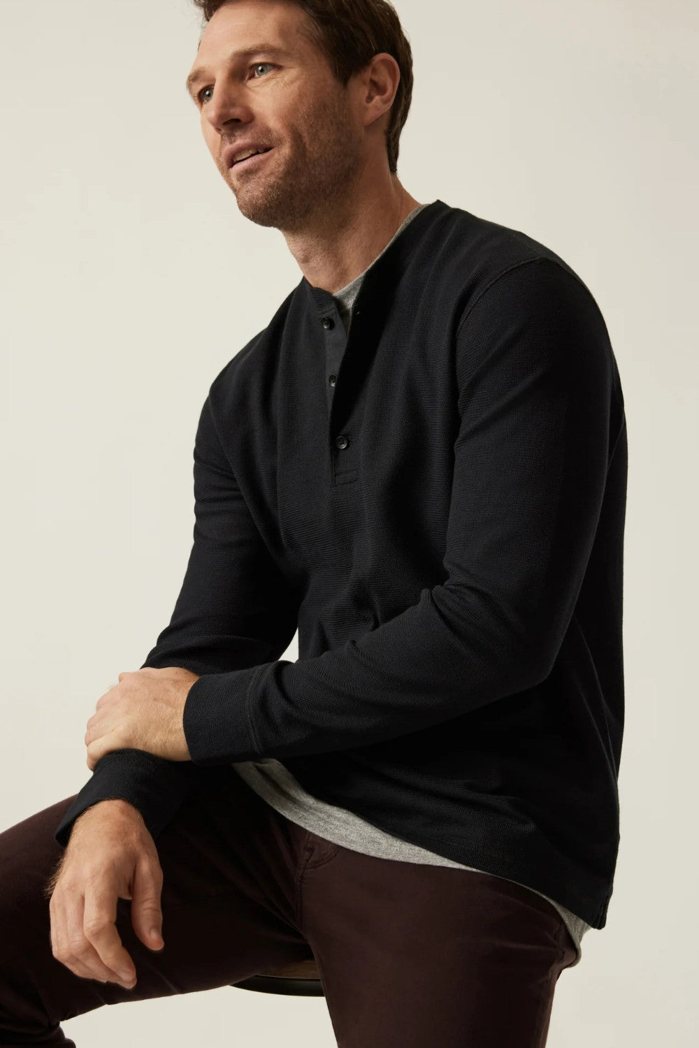 Man wearing a black long-sleeve shirt sitting against a plain background