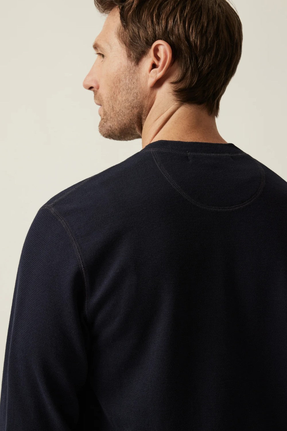 Man wearing a navy blue sweater against a beige background