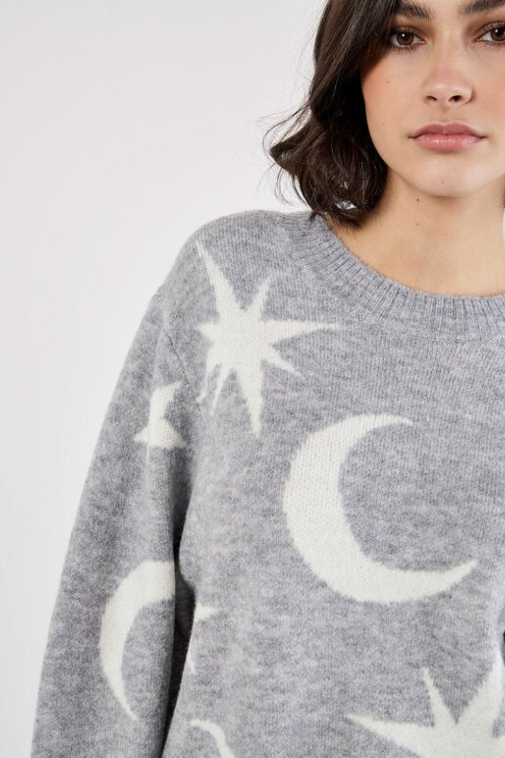 Person wearing a gray sweater with star and moon patterns on a white background