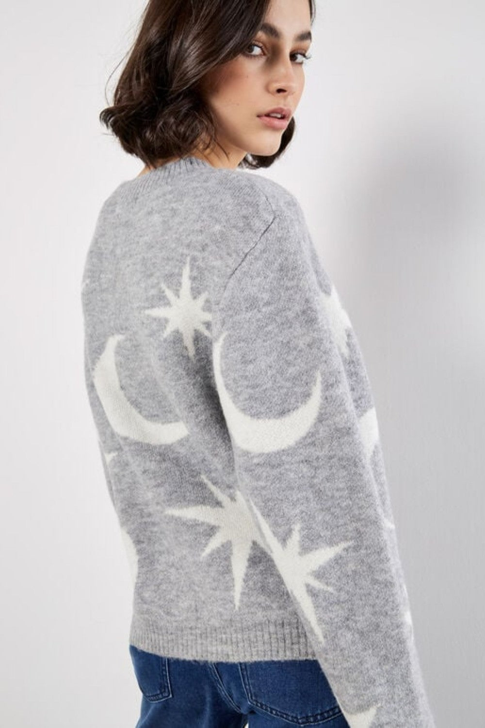 Person wearing a gray sweater with star and moon designs on a plain background