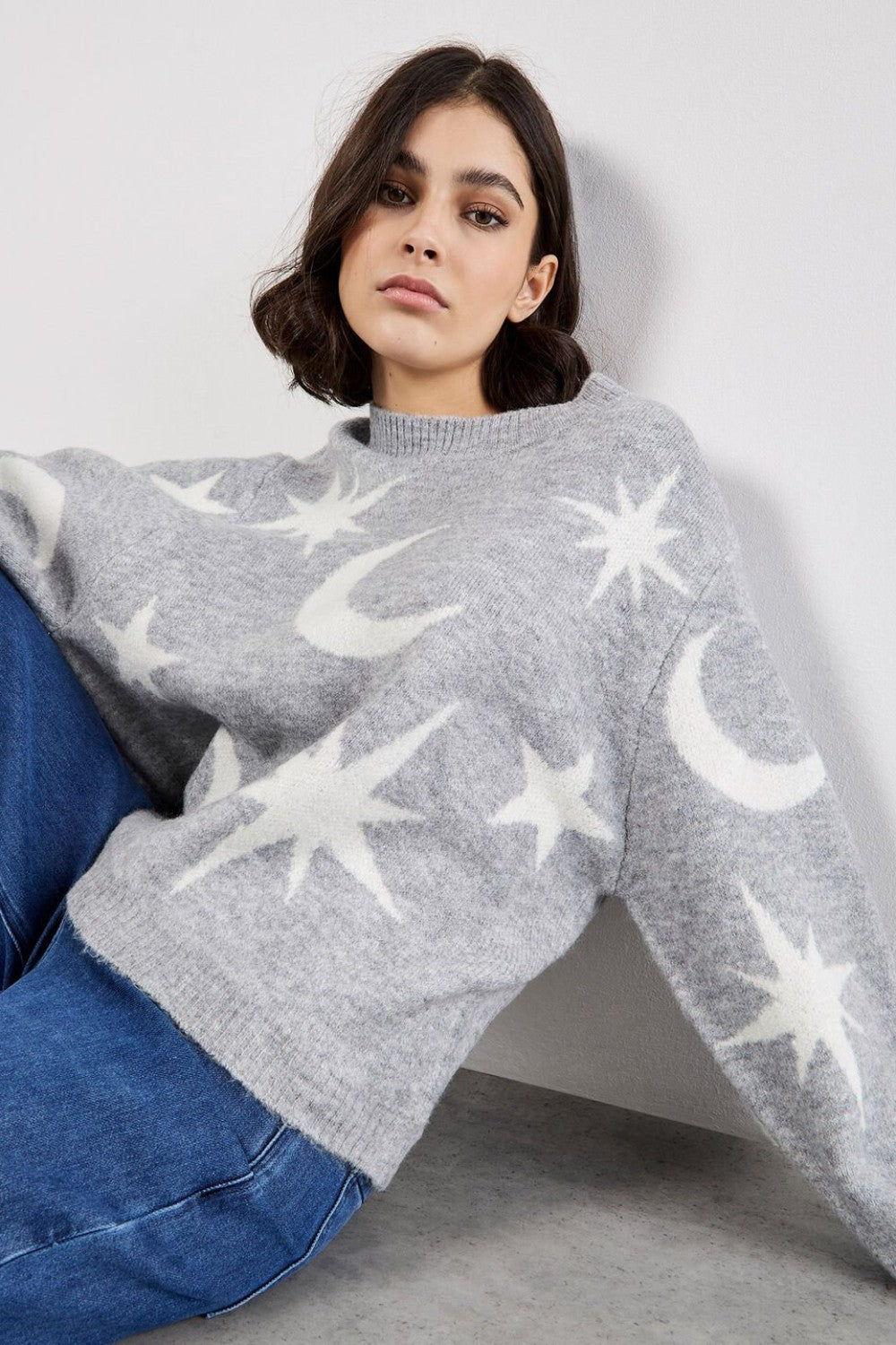 Woman wearing a gray sweater with star and moon patterns against a plain background