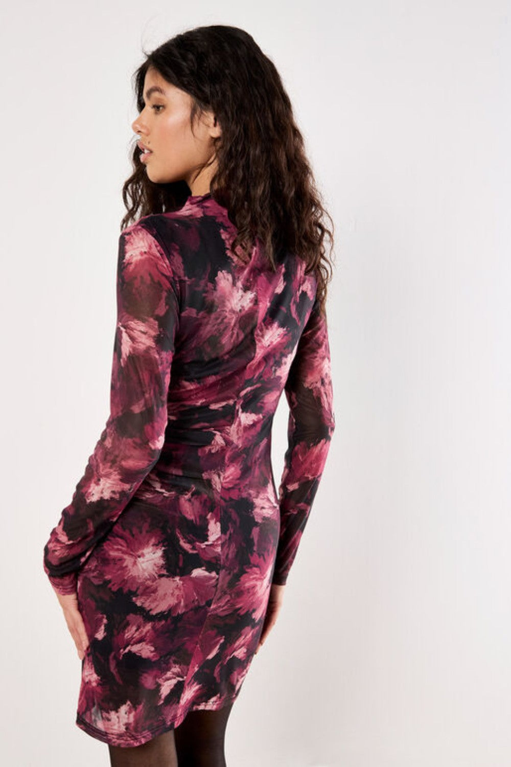 Woman wearing a long-sleeve, patterned dress against a white background