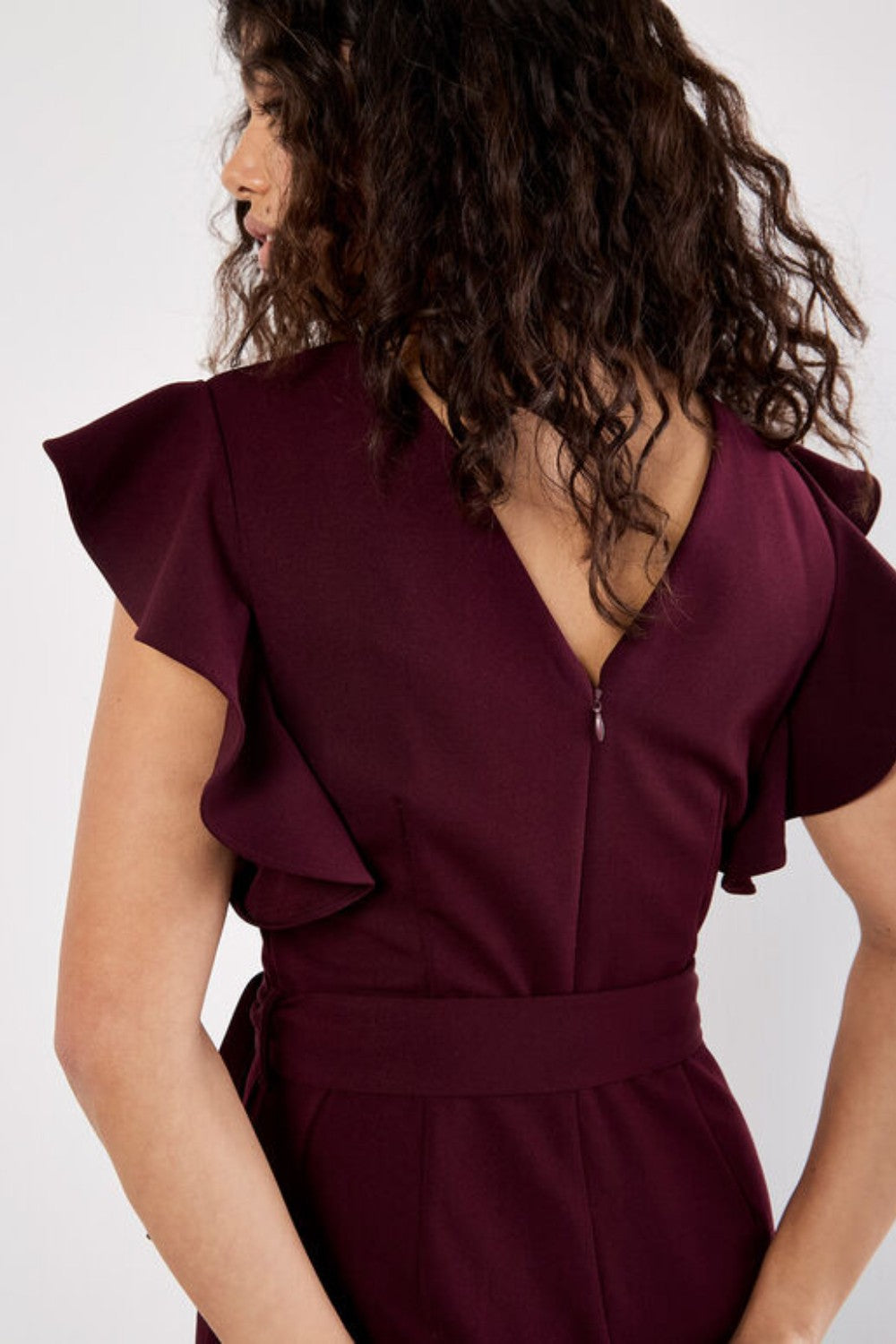 Woman wearing a burgundy jumpsuit with ruffled sleeves against a white background