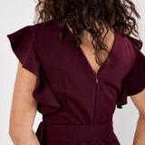 Woman wearing a burgundy jumpsuit with ruffled sleeves against a white background
