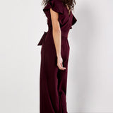 Woman wearing a burgundy jumpsuit with ruffled sleeves against a white background