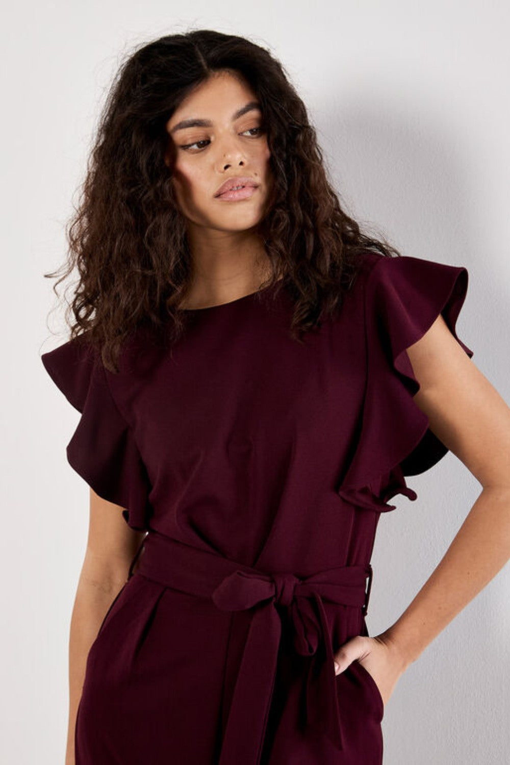 Woman wearing a burgundy jumpsuit with ruffled sleeves against a white background