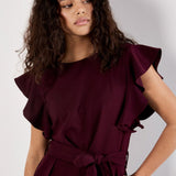 Woman wearing a burgundy jumpsuit with ruffled sleeves against a white background
