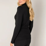 Woman wearing a black long-sleeve top and black pants against a plain background