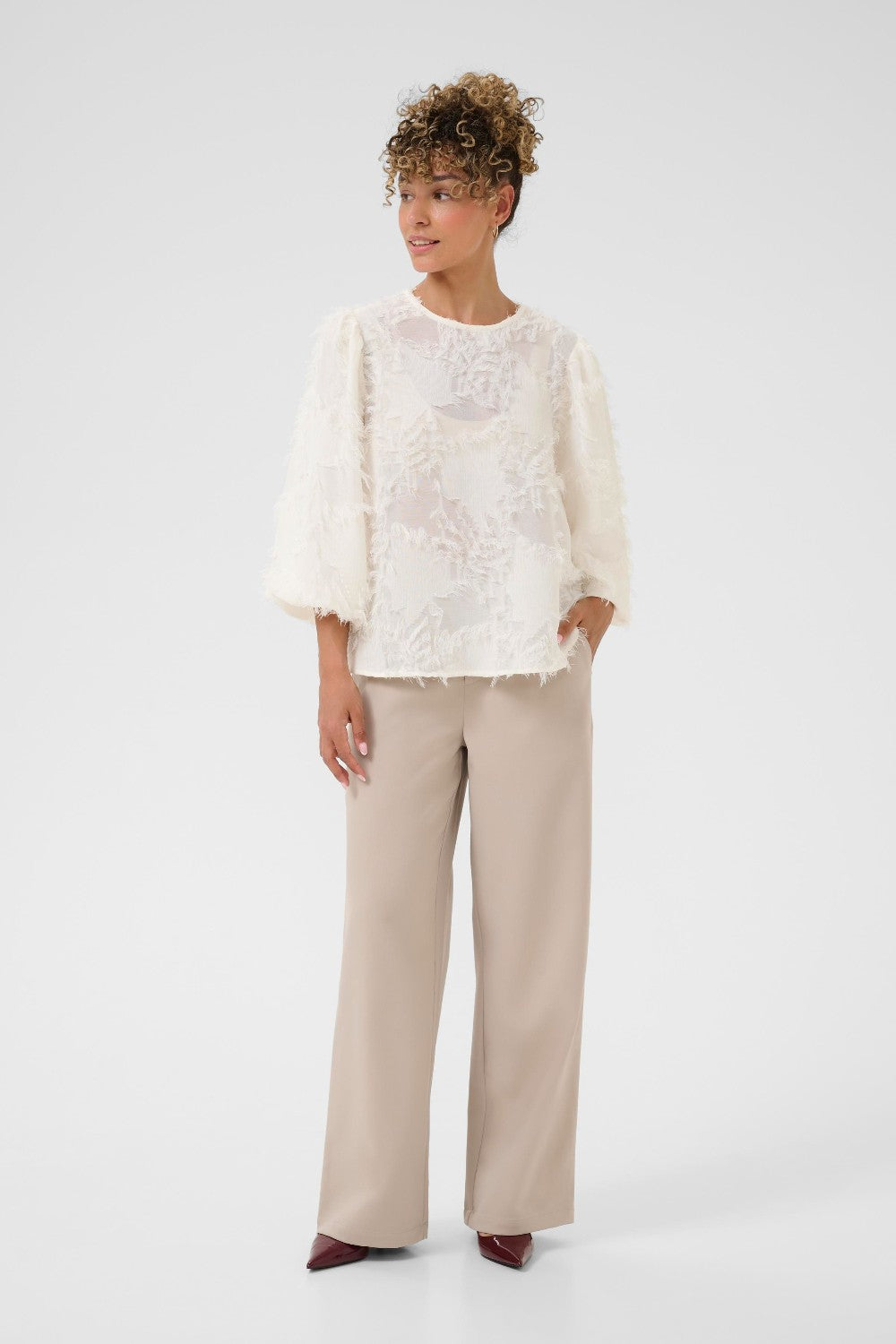 Woman wearing a white lace top and beige pants on a white background