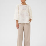 Woman wearing a white lace top and beige pants on a white background