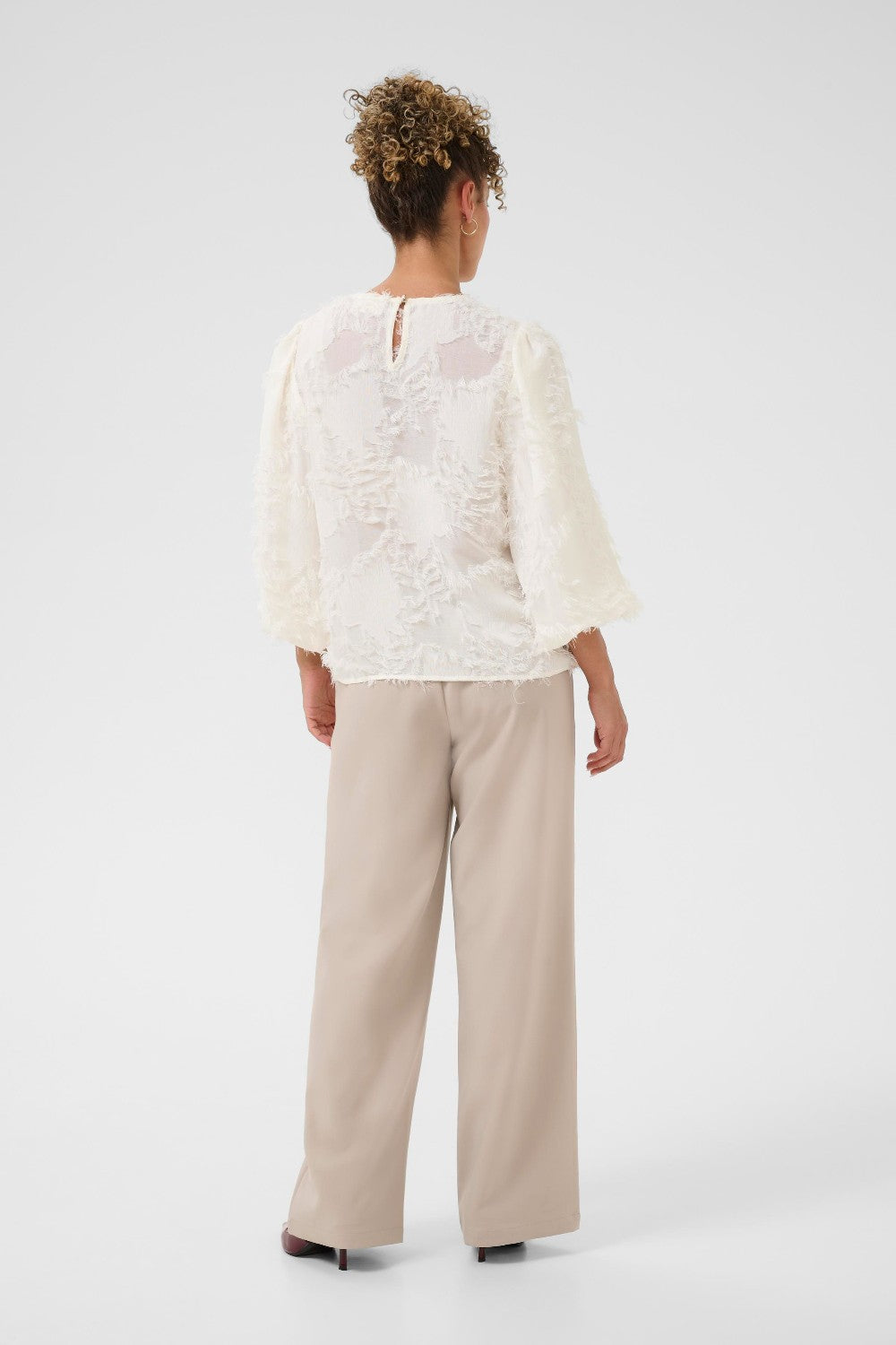Person wearing a white lace top and beige pants on a white background