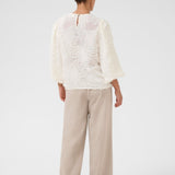 Person wearing a white lace top and beige pants on a white background