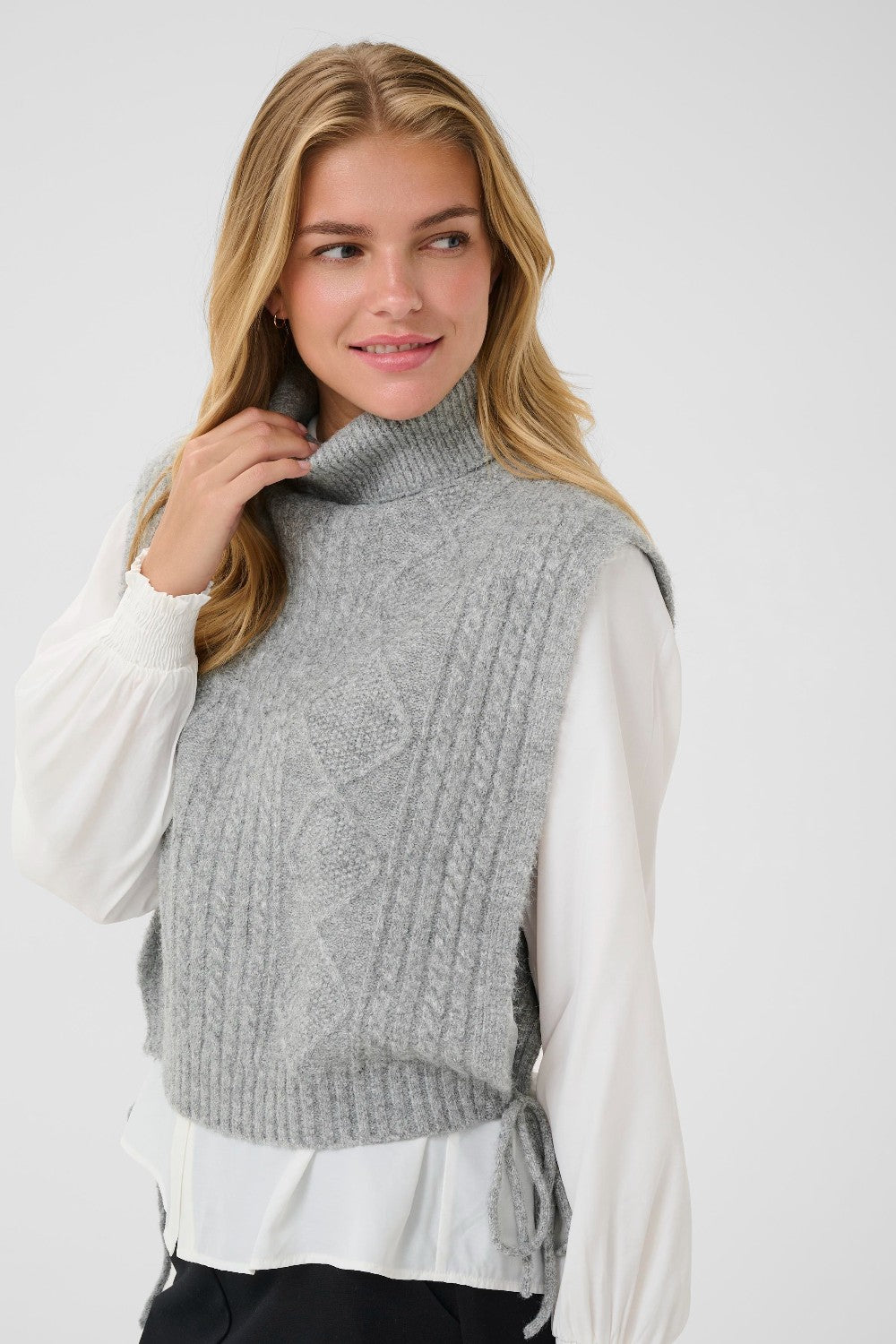 Woman wearing a gray knitted vest over a white shirt on a white background