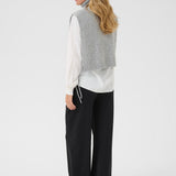 Woman wearing a gray knitted vest over a white shirt with black pants on a white background