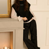 Woman in stylish outfit leaning against a fireplace with candles.