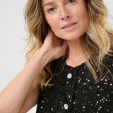 Woman wearing a black sequined vest against a plain background