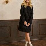 Woman in a black dress standing in an elegant room with decorative wall and floor.