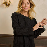 Woman wearing a black dress with floral details in an indoor setting