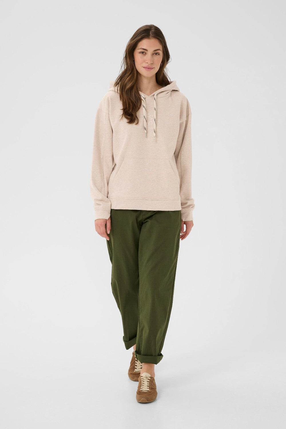Woman wearing a beige hoodie and green pants on a white background