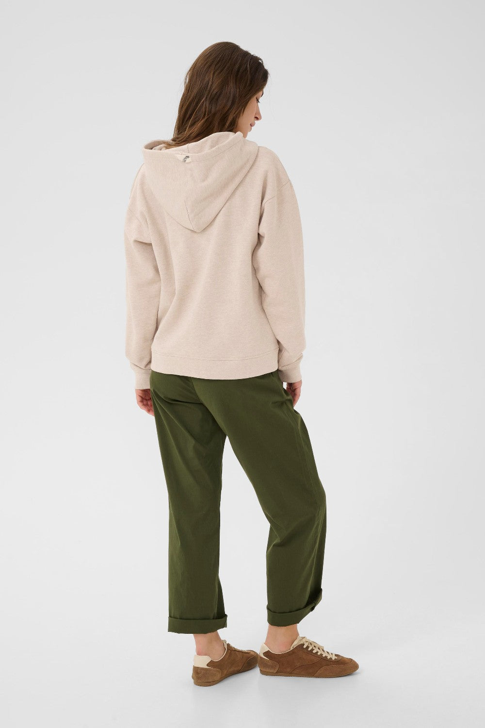 Person wearing a beige hoodie and green pants on a white background