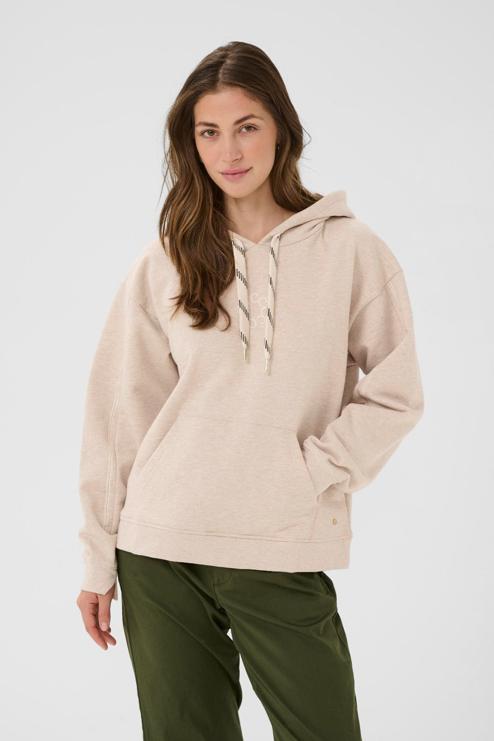 Woman wearing a beige hoodie and green pants on a white background