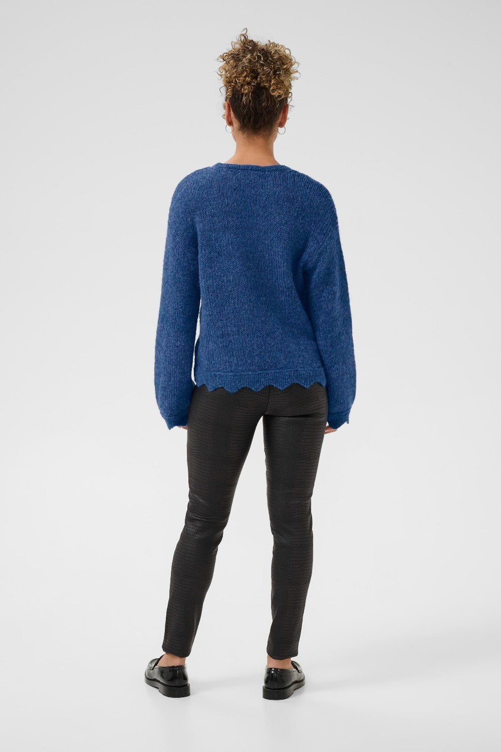 Person wearing a blue sweater and black pants on a white background