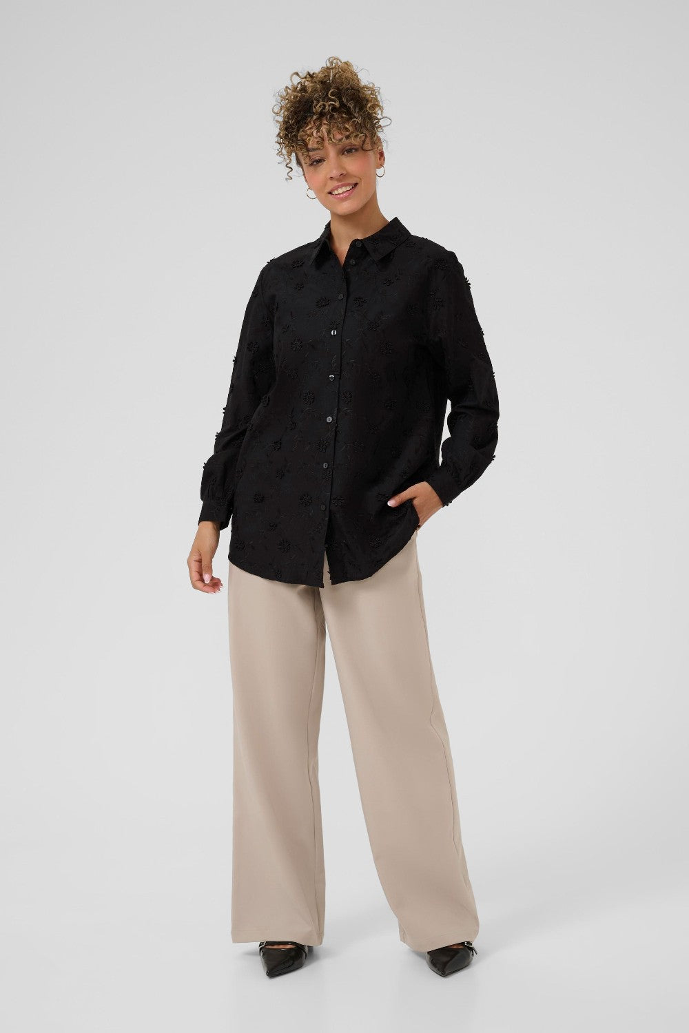 Person wearing a black shirt and beige pants on a white background