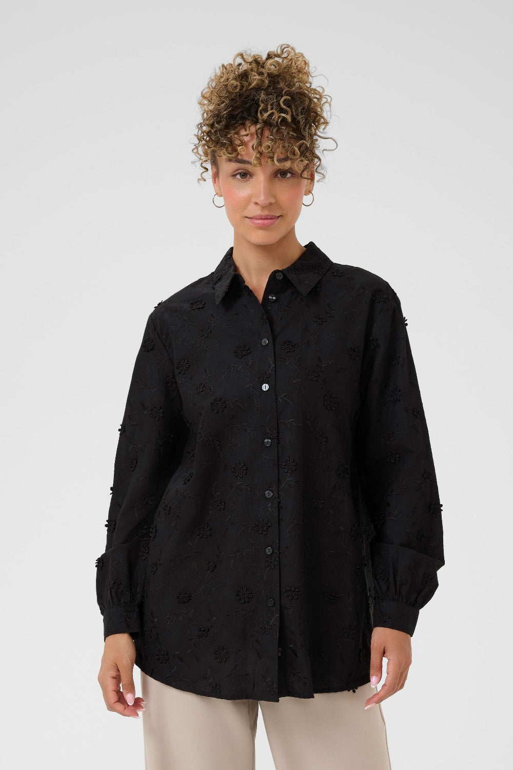 Woman wearing a black button-up shirt with a subtle pattern on a white background