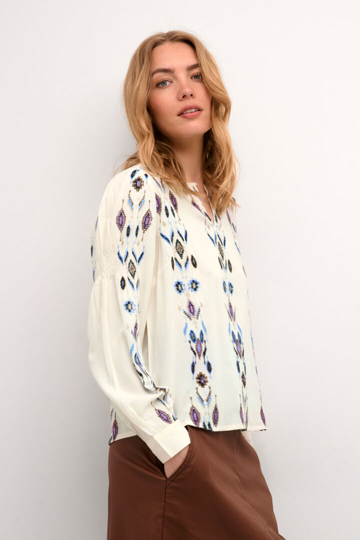 The Cream Polly Blouse features an ethnic square blue print, making it perfect for adding a touch of global-inspired style to your wardrobe. With a keyhole at the neck and button closure, this versatile piece is also denim friendly for effortless, on-trend outfits.