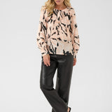Woman wearing a patterned blouse and black pants on a white background