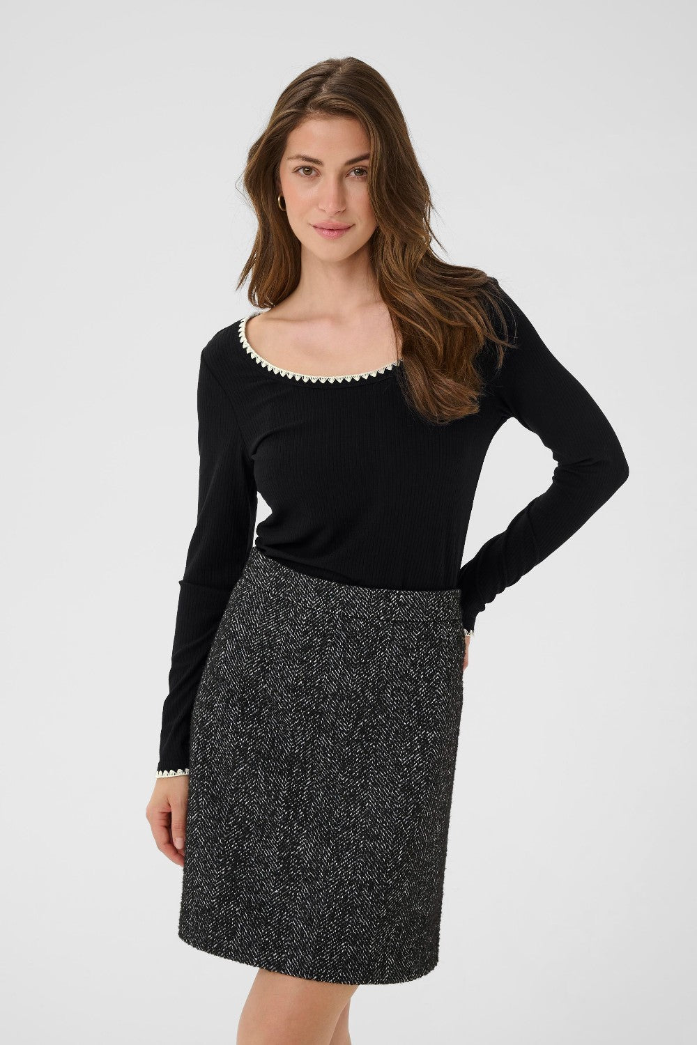 Woman wearing a black long-sleeve top and patterned skirt on a white background