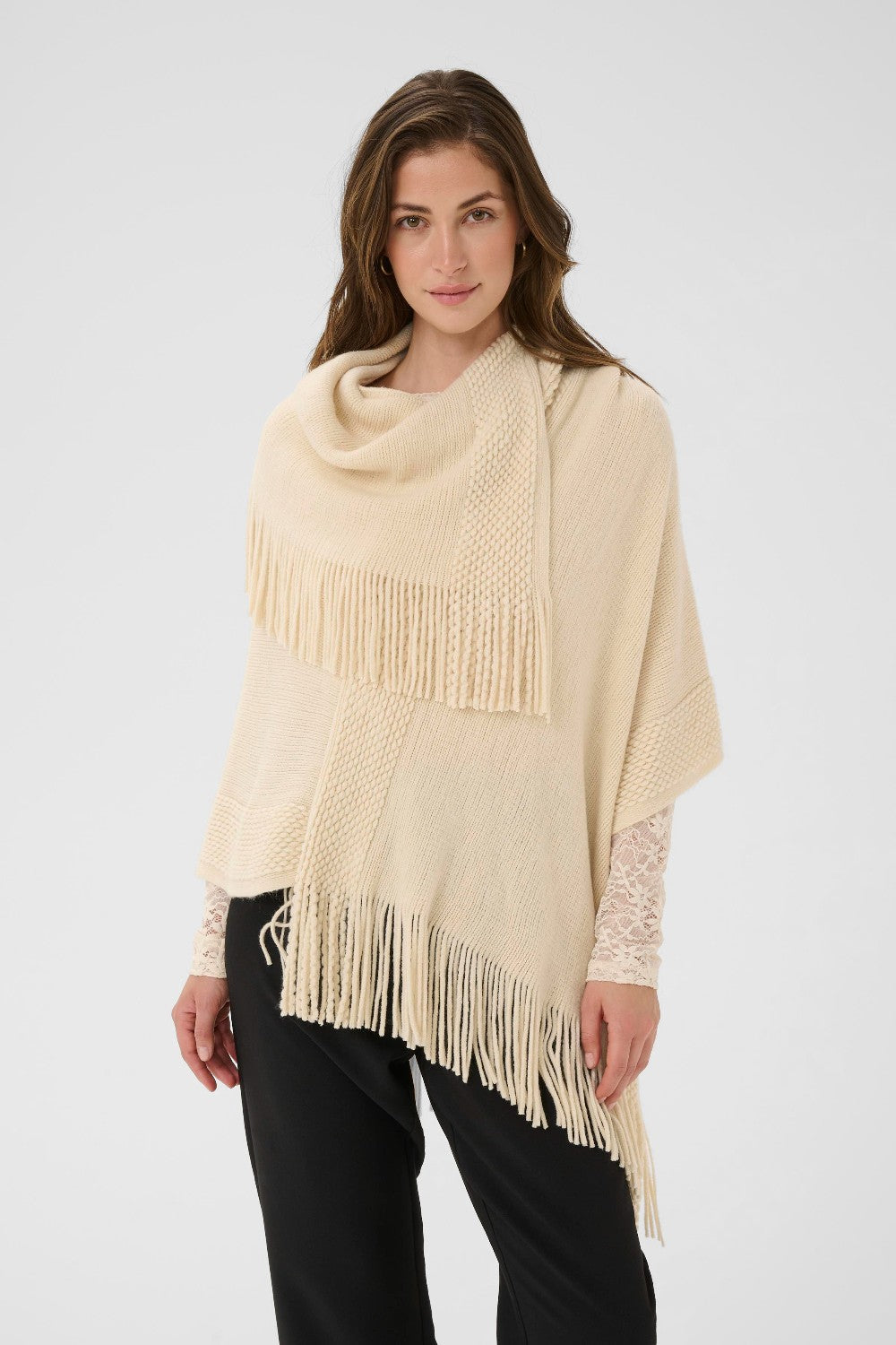 Woman wearing a beige poncho with fringe details on a white background