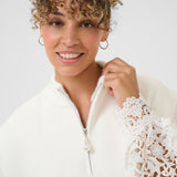 Woman wearing a white vest and blouse with lace sleeves against a plain background