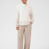 Woman wearing a white vest and blouse with lace sleeves and beige pants on a white background
