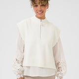 Woman wearing a white vest and blouse with lace sleeves and trim on a plain background