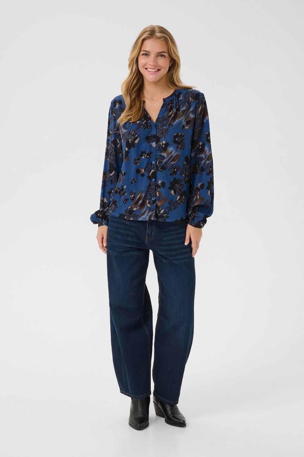 Woman wearing a blue floral blouse and dark jeans on a white background