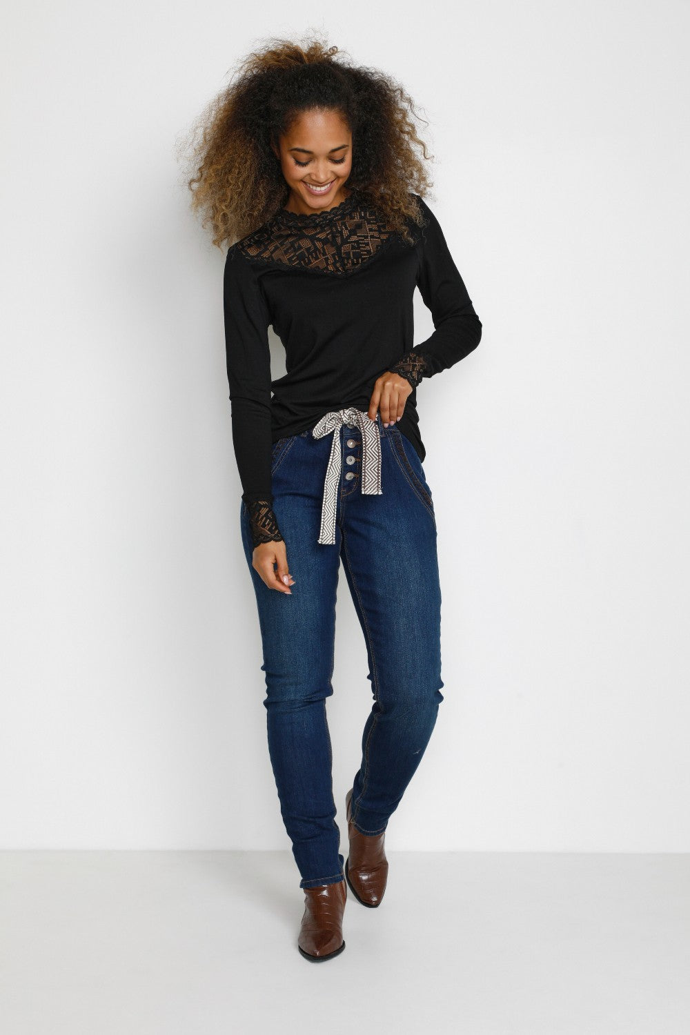 Woman wearing a black top, blue jeans, and brown shoes on a white background