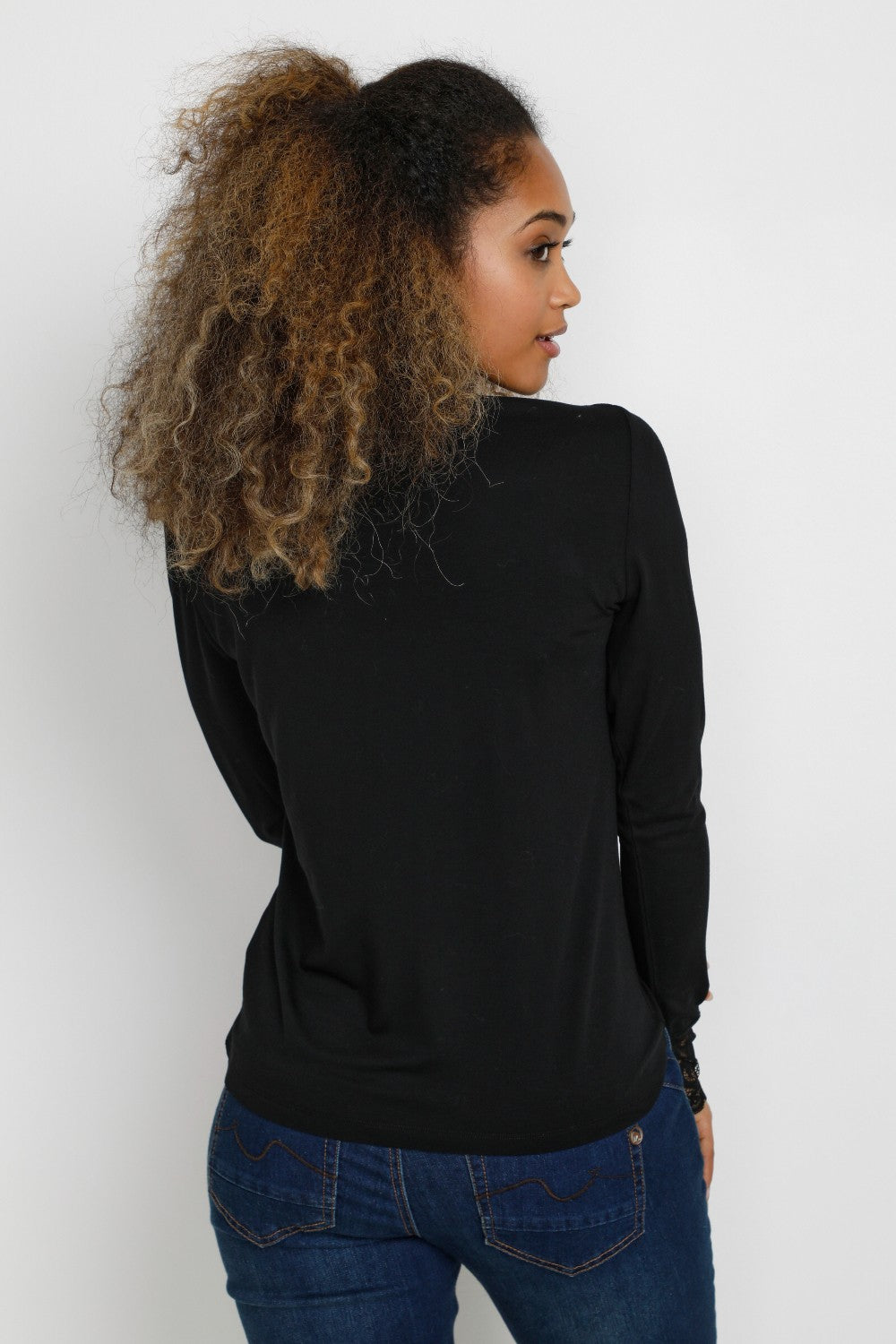 Woman wearing a black long-sleeve top and blue jeans against a white background