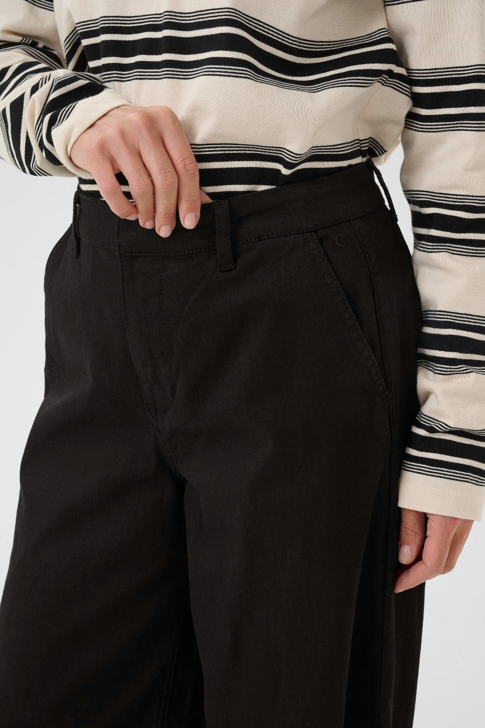 Person wearing a striped shirt and black pants on a white background