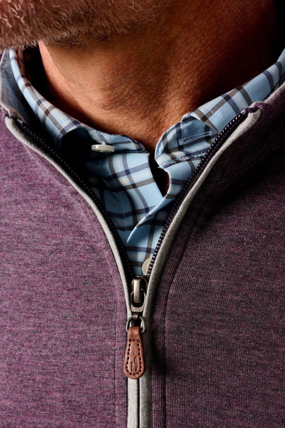 Close-up of a person wearing a purple zip-up sweatshirt over a plaid shirt.