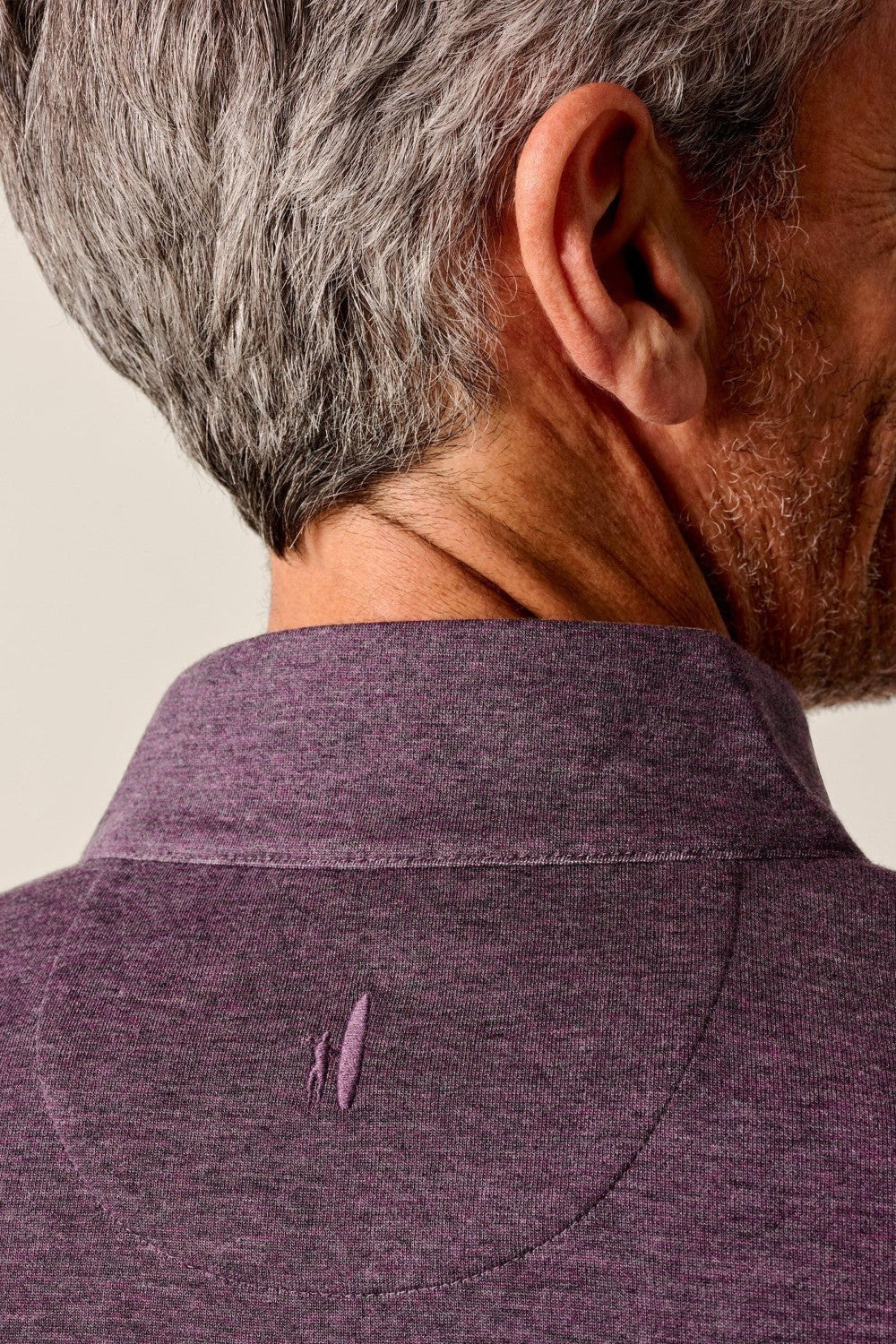 Close-up of a person wearing a purple shirt with a brand logo on a plain background