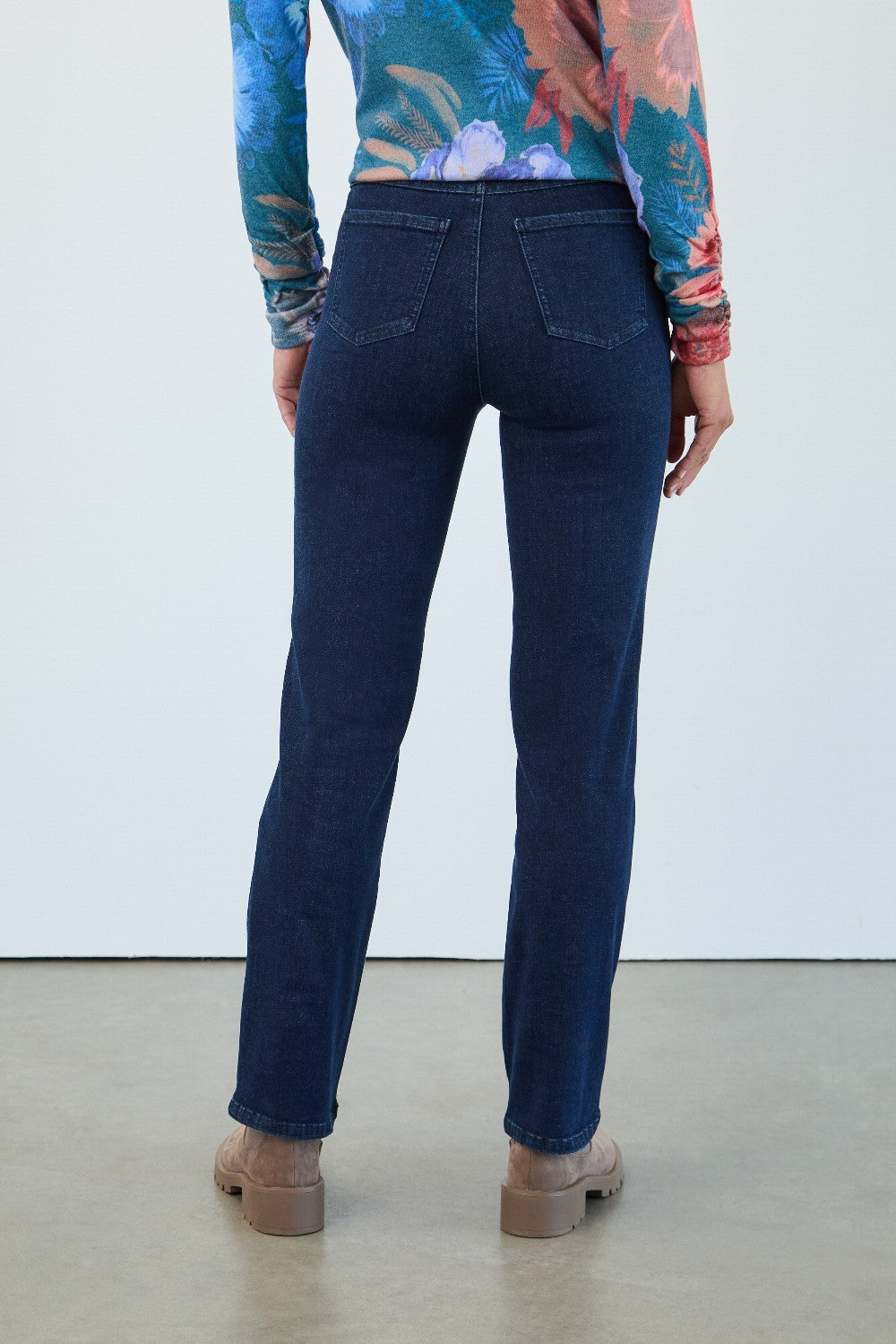 Person wearing blue jeans and a colorful top on a plain background