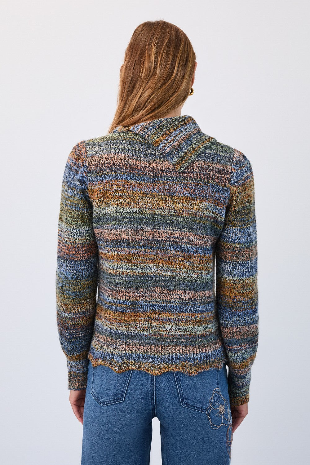 Person wearing a multicolored patterned sweater and blue jeans on a white background