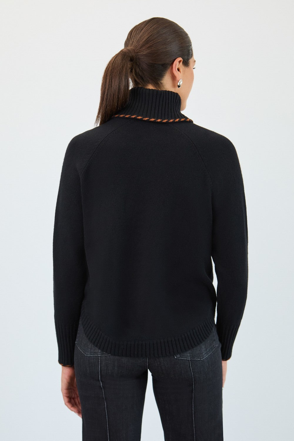 Person wearing a black turtleneck sweater and dark jeans on a white background