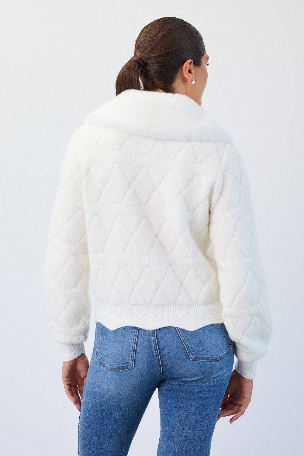 Person wearing a white quilted jacket and blue jeans on a light gray background