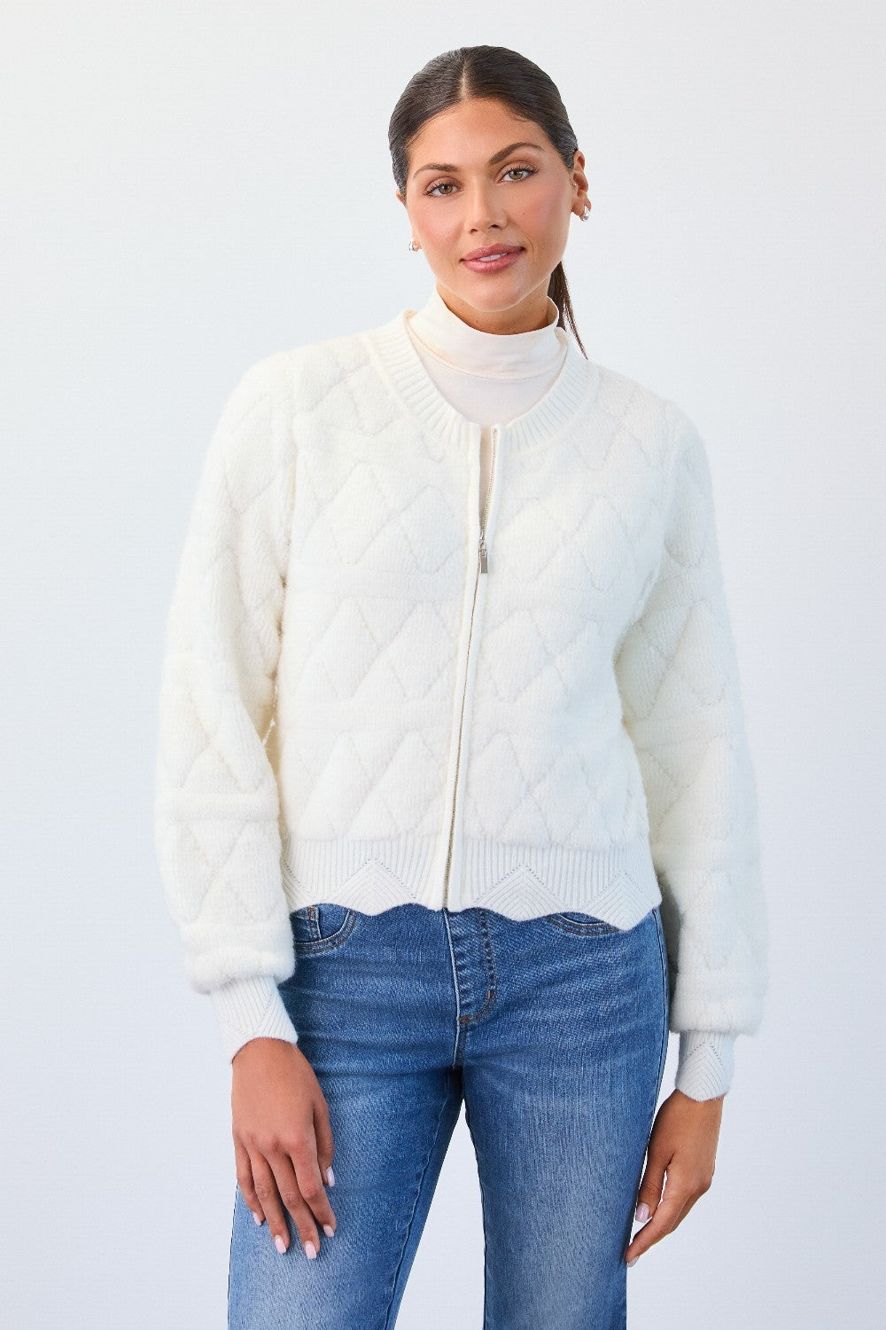 Woman wearing a white zip-up sweater over a turtleneck with blue jeans on a light gray background