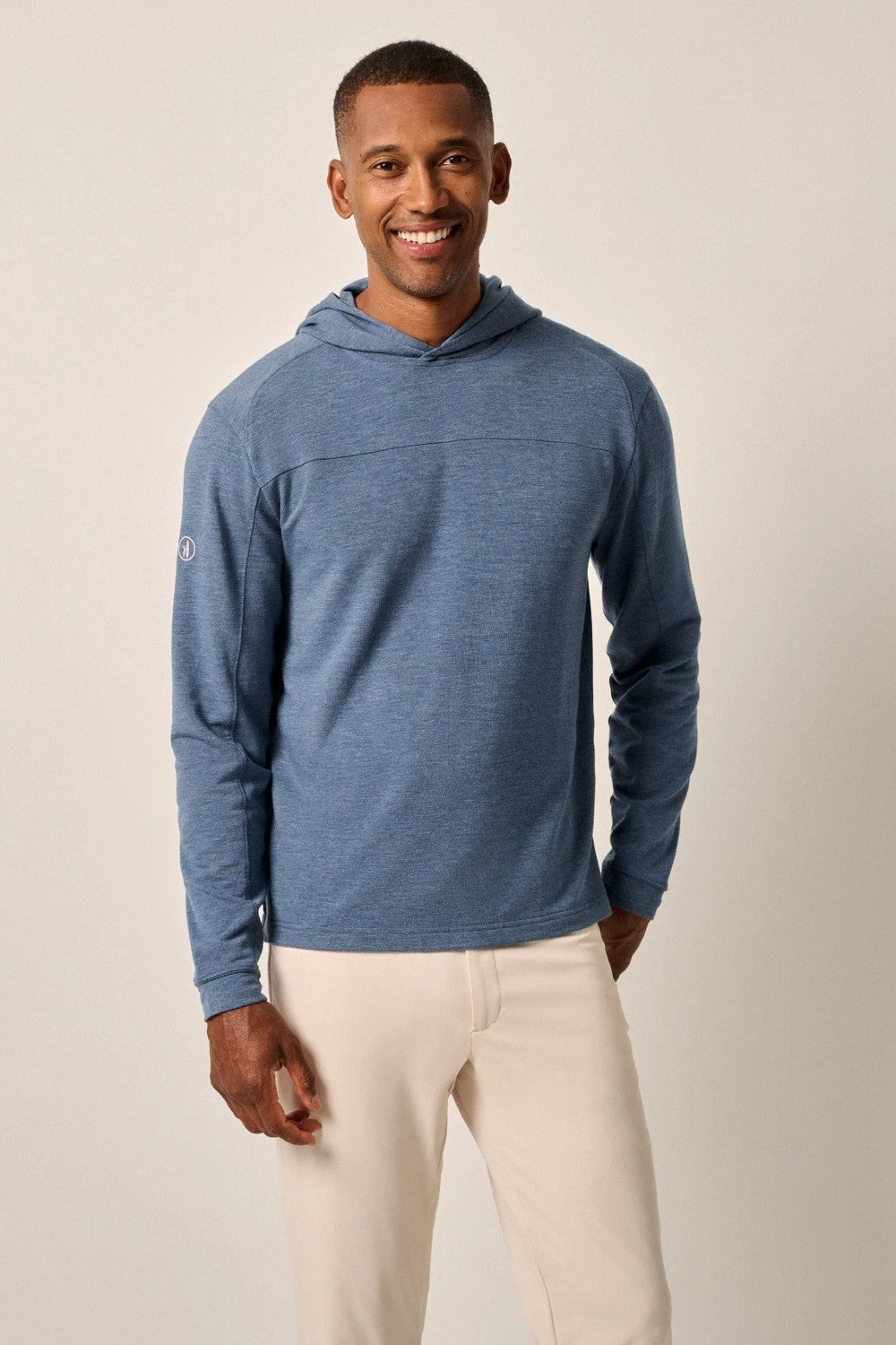 Man wearing a blue hoodie and white pants against a beige background
