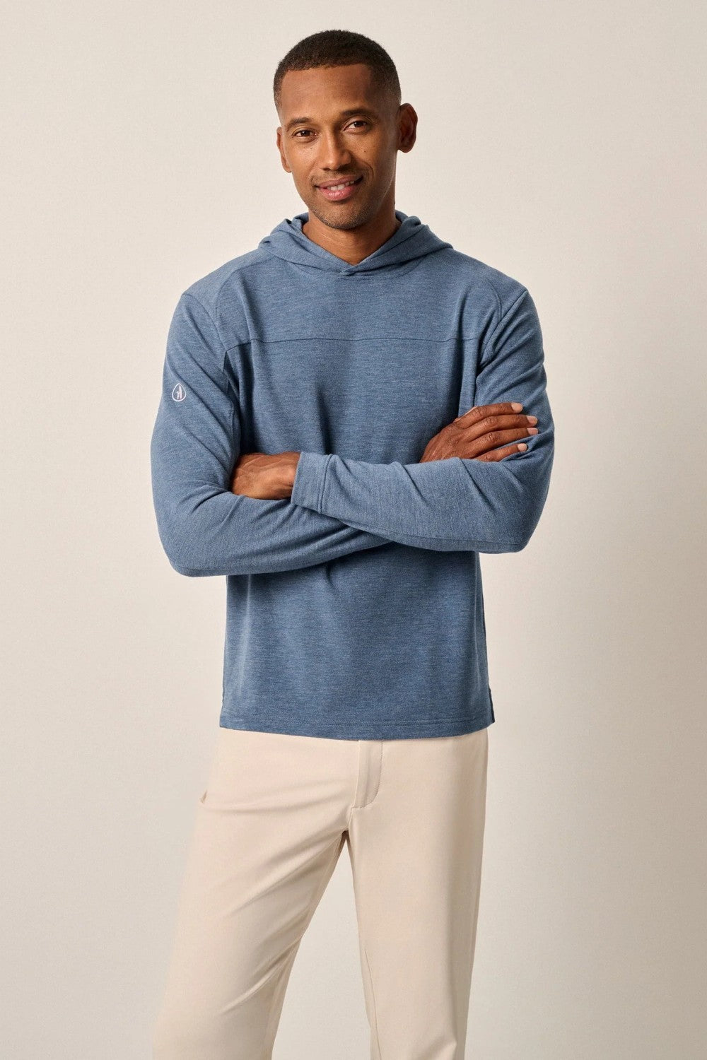 Man wearing a blue hoodie and beige pants against a plain background